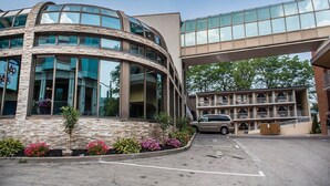 A modern building with a curved glass facade, a parking area, and a multi-story structure with balconies. - Quality Hotel Fallsview Cascade (Niagara Falls)