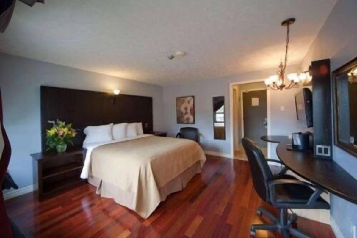 A hotel room with a bed, desk, and chair, wooden flooring, and a chandelier.
