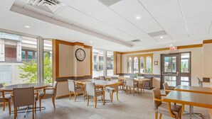 A spacious dining area with multiple tables and chairs, a clock on the wall, and large windows allowing natural light. - Quality Hotel Fallsview Cascade (Niagara Falls)