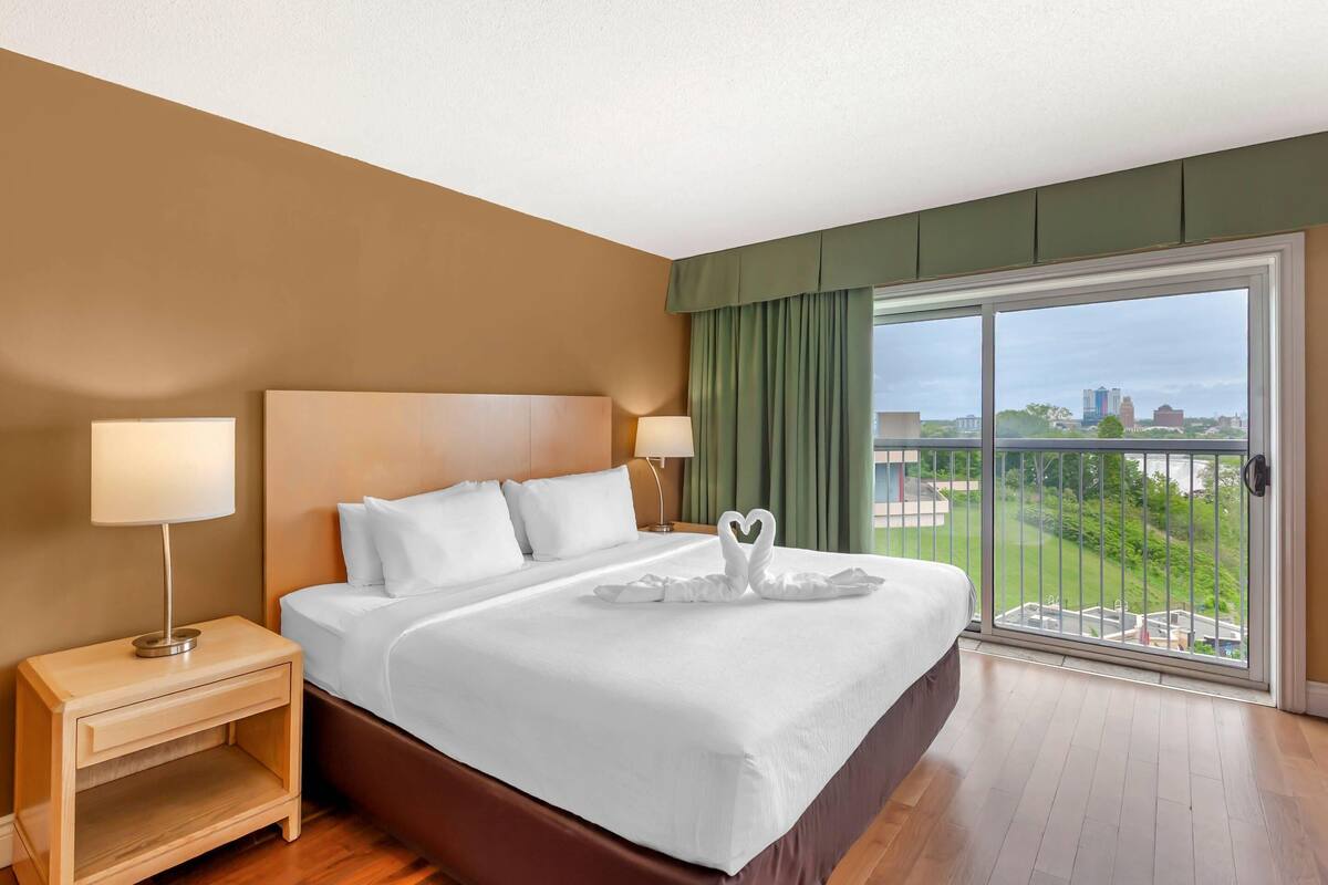 A hotel room with a large bed, two bedside tables, a view of the city through a sliding glass door.