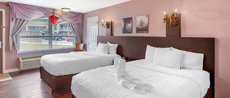 A hotel room with two beds, a large window with curtains, a view of the street, and wall-mounted sconces.