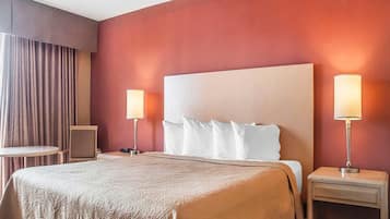A hotel room with a large bed, two bedside tables with lamps, a small round table, and a chair.