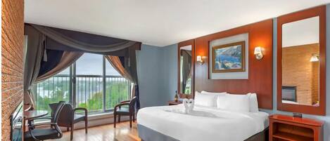 Une chambre d’hôtel avec un grand lit, un bureau et une chaise. Il y a une fenêtre avec des rideaux, un tableau au mur et un miroir.