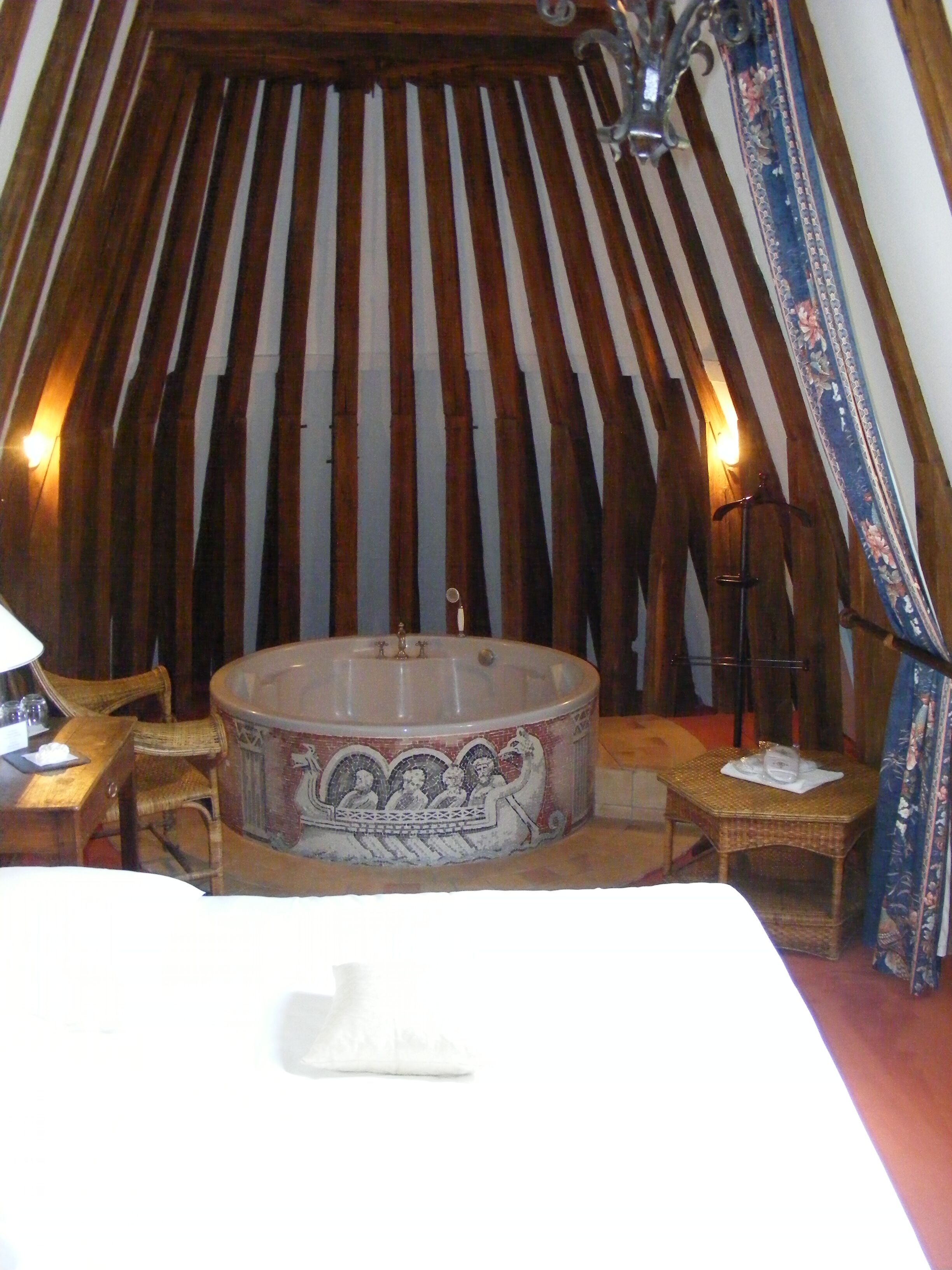 A room with a large bathtub, wicker furniture, and a curtain with a floral pattern.