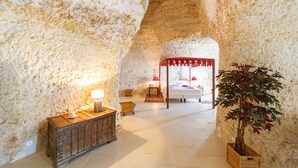 Une chambre aux murs de pierre, dotée d’un lit à baldaquin, d’une table de chevet avec une lampe et d’une plante en pot.