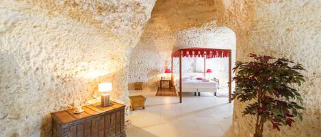 Un dormitorio con paredes de piedra, una cama con dosel, una mesita de noche con lámpara y una planta en maceta.