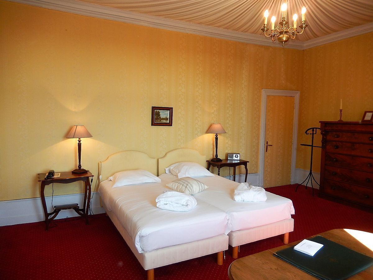 A hotel room with two beds, a wooden dresser, a desk, and a chandelier.