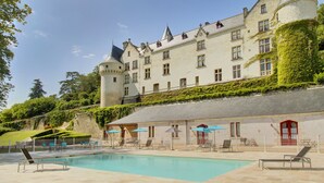 Un gran edificio de estilo castillo con piscina, sillones de descanso y sombrillas.