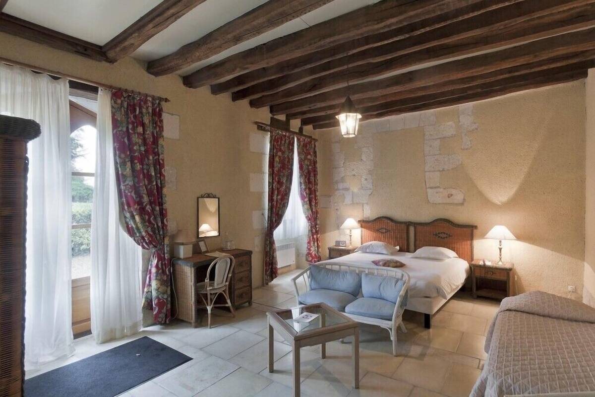 Une chambre à coucher comprenant un lit, deux tables de chevet, une chaise, une petite table et une fenêtre avec des rideaux.