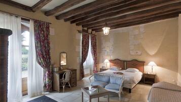 Un dormitorio con una cama, dos mesitas de noche, una silla, una pequeña mesa y una ventana con cortinas.