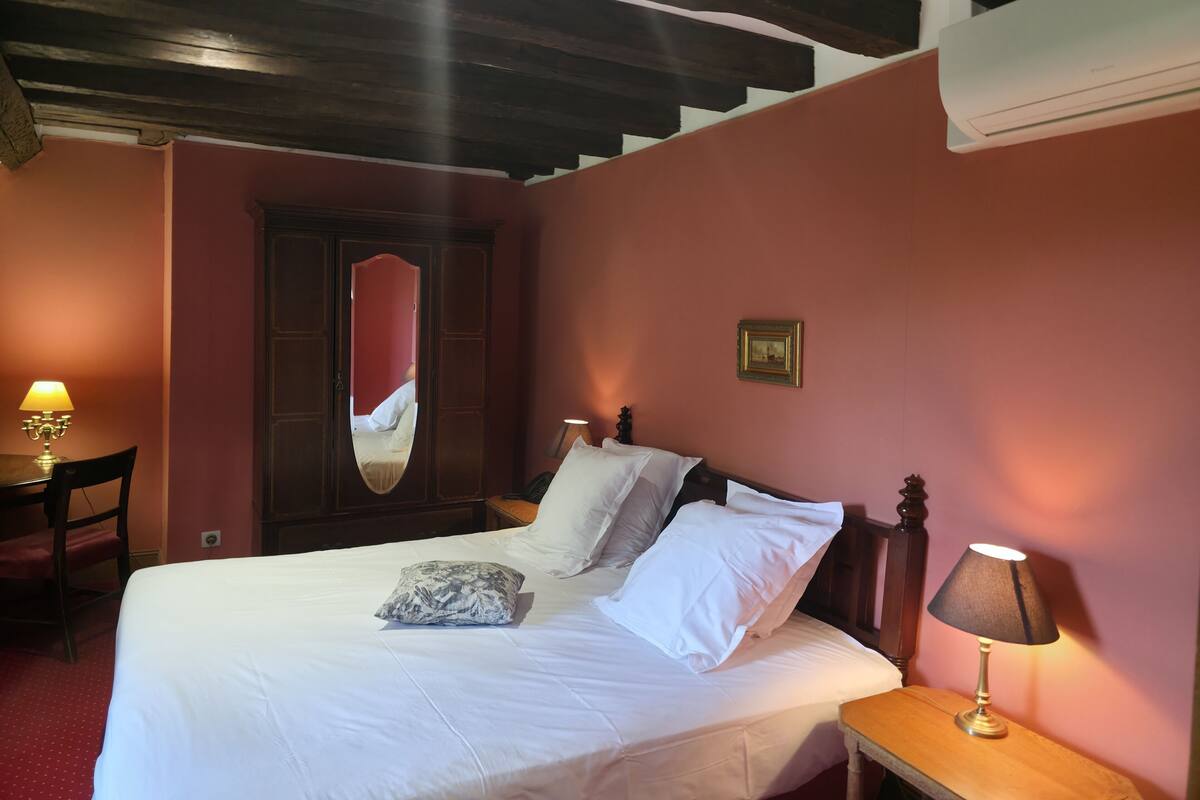 Une chambre à coucher avec un lit, une table de chevet, une lampe, un miroir et une porte.