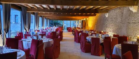 A restaurant with tables set for dining, wooden beams on the ceiling, and a stone wall.