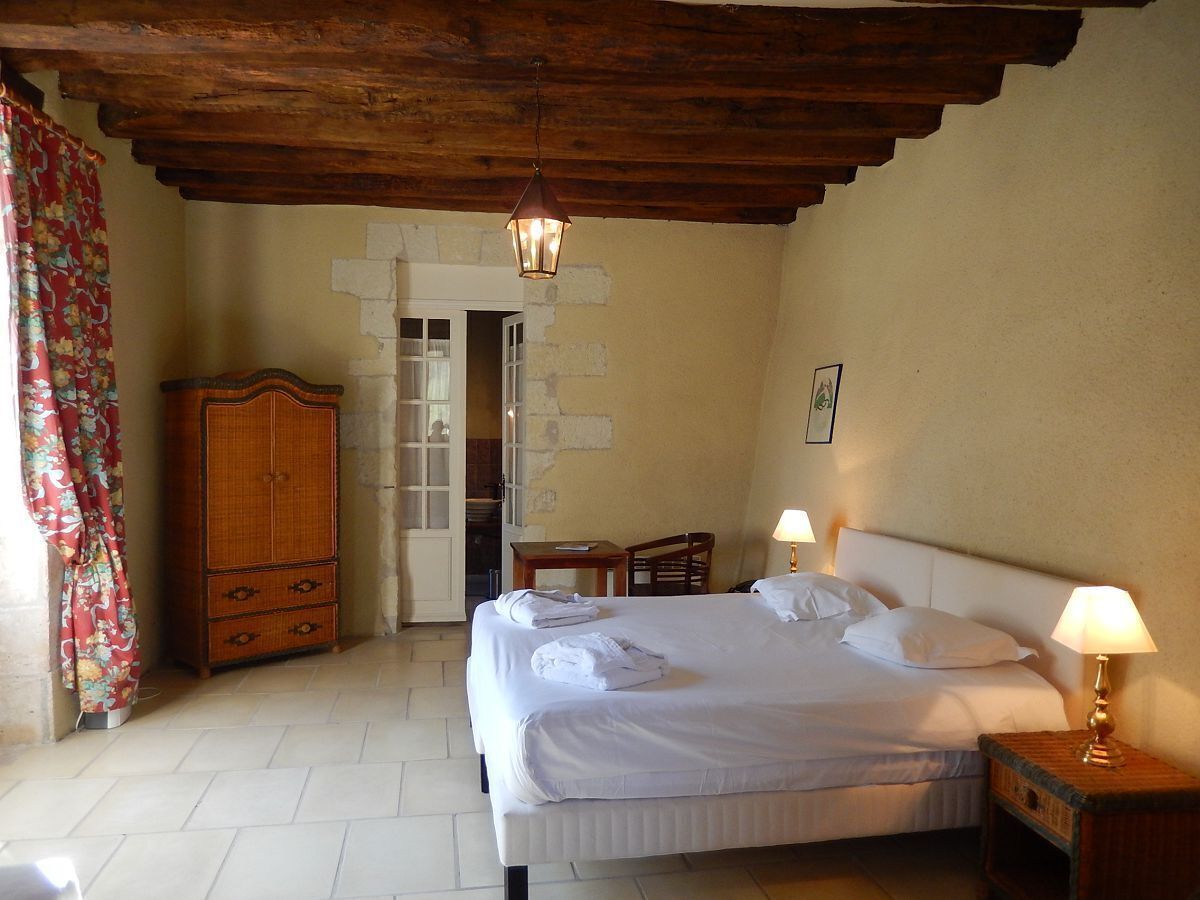 A bedroom with a bed, two bedside lamps, a wooden wardrobe, and a door leading to another room.