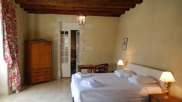 A bedroom with a bed, two bedside lamps, a wooden wardrobe, and a door leading to another room.