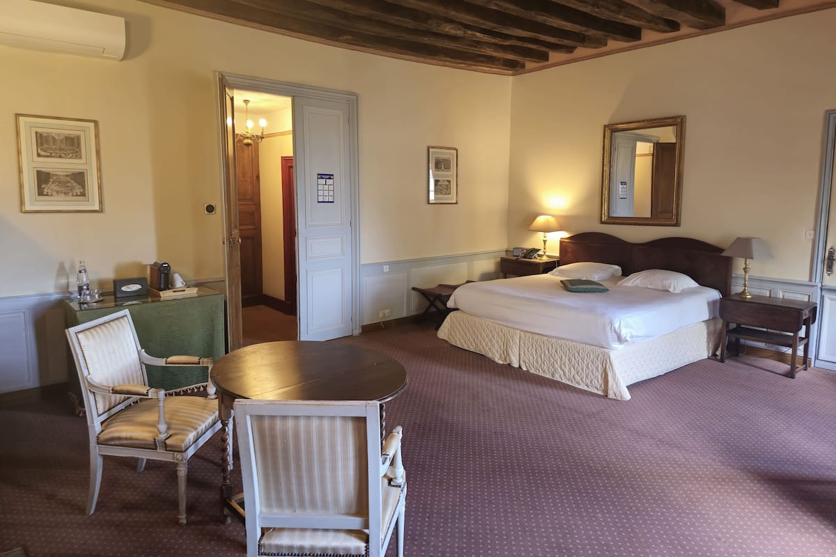 Une chambre d’hôtel comprenant un lit, une table de chevet, une lampe, une chaise et un bureau avec une autre chaise.