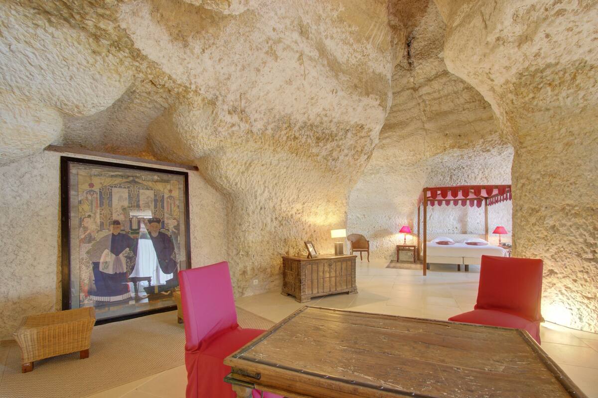 Une pièce avec un grand tableau, une table en bois et des chaises rouges.