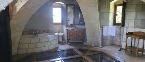A stone-walled bathroom with a bathtub, sink, and wooden vanity.