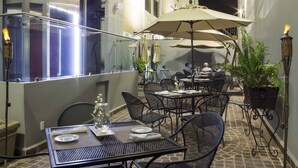 An outdoor dining area with tables and chairs, umbrellas, and a potted plant.
