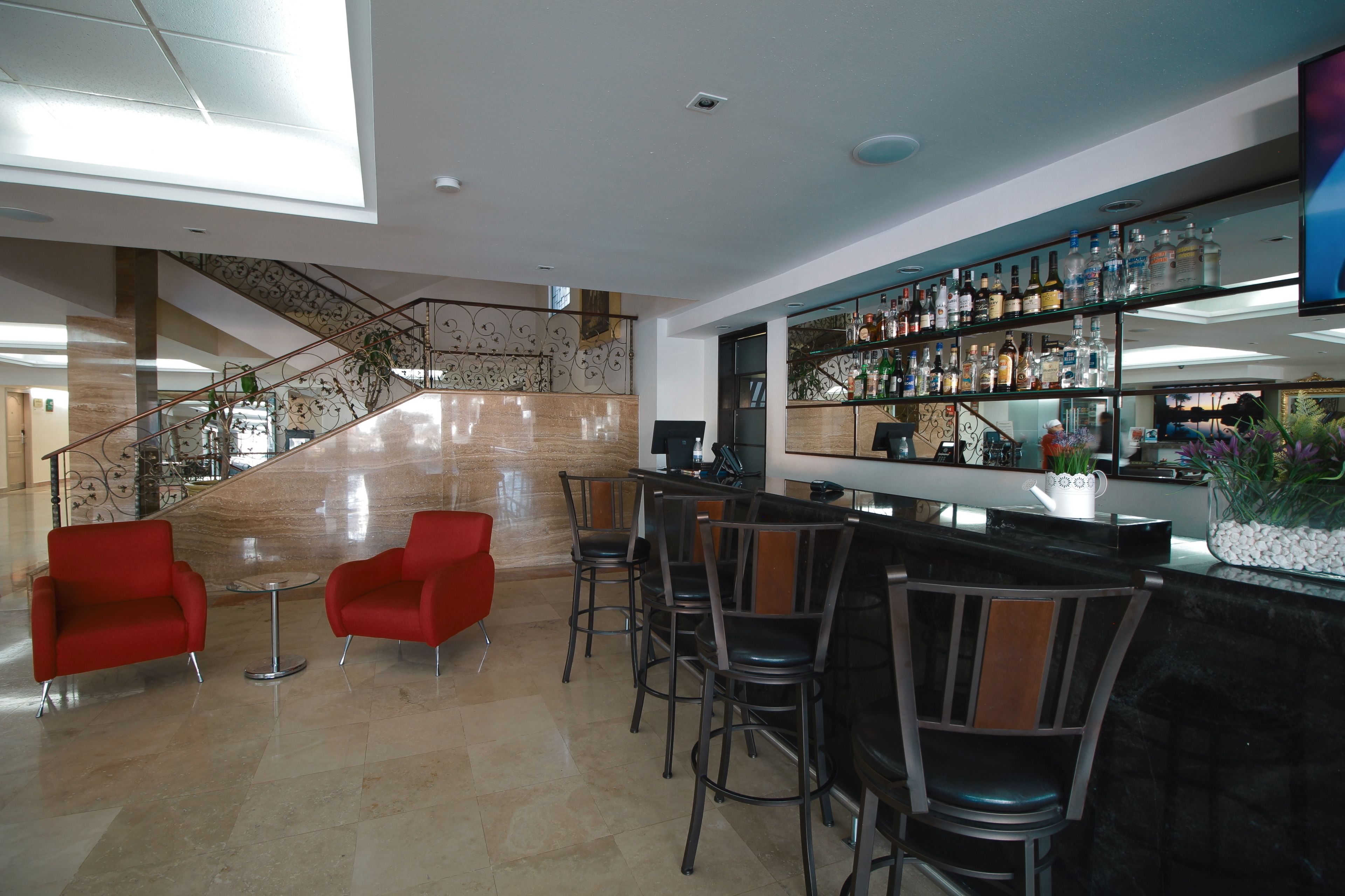 A modern lobby with a bar area, red chairs, a staircase, and a glass railing.