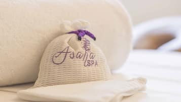 A neatly folded towel with "Asana Spa" embroidered on it, placed on a bed.