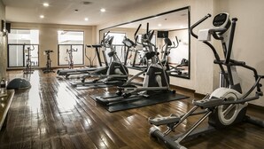 A gym with multiple cardio machines, wooden floors, and large windows.