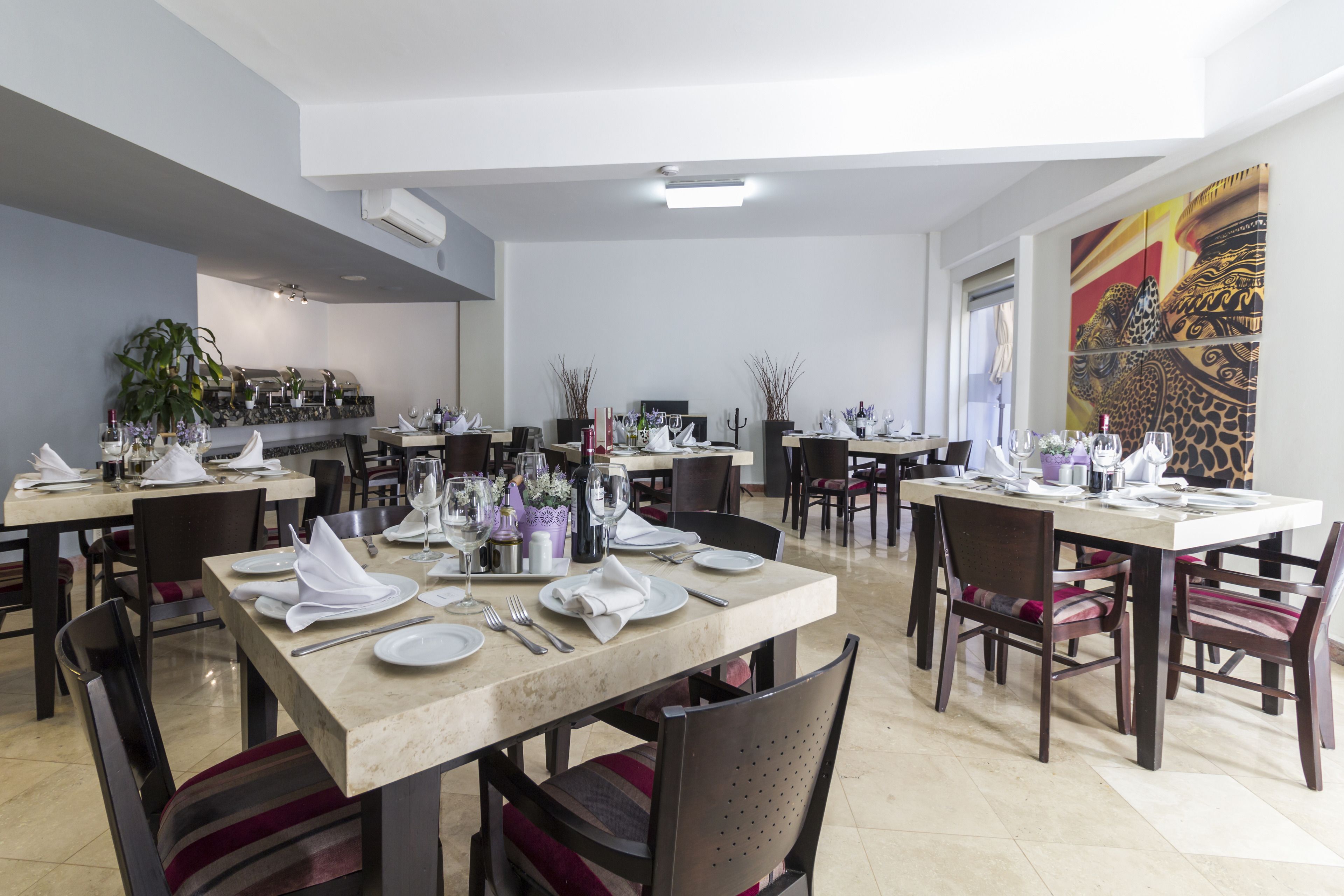 Un comedor espacioso con varias mesas dispuestas para comer, sillas y un cuadro decorativo grande en la pared.