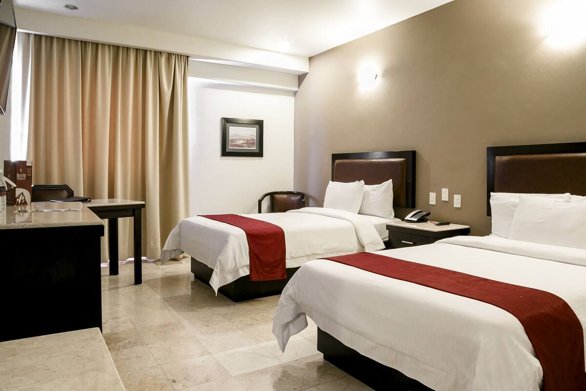 A hotel room with two beds, a desk, a chair, a telephone, and a picture on the wall.
