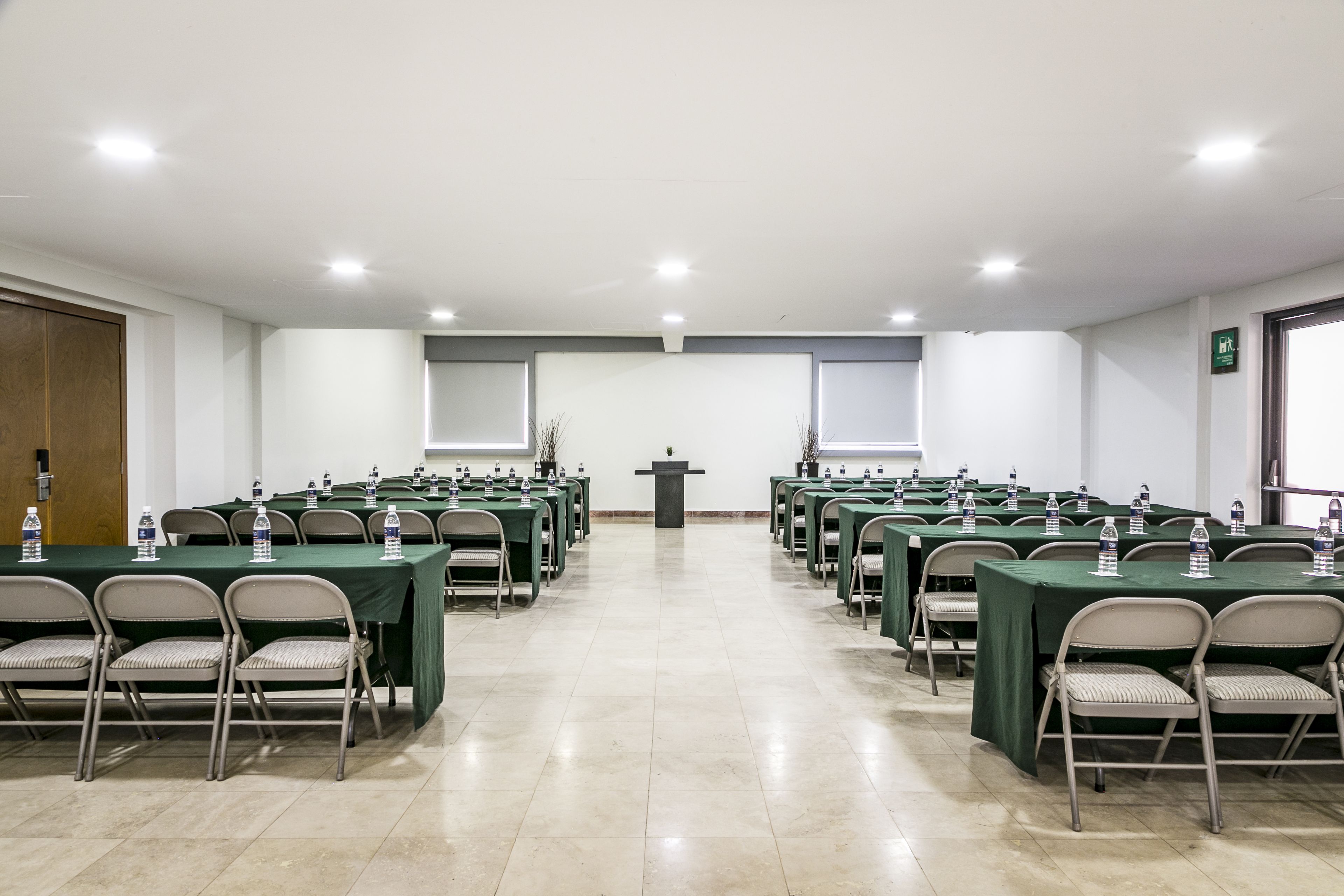 A conference room with multiple tables and chairs, a podium, and water bottles on each table.