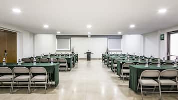 A conference room with multiple tables and chairs, a podium, and water bottles on each table.