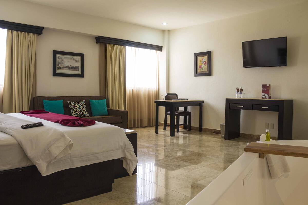 A hotel room with a bed, a desk, a television, and a window with curtains.