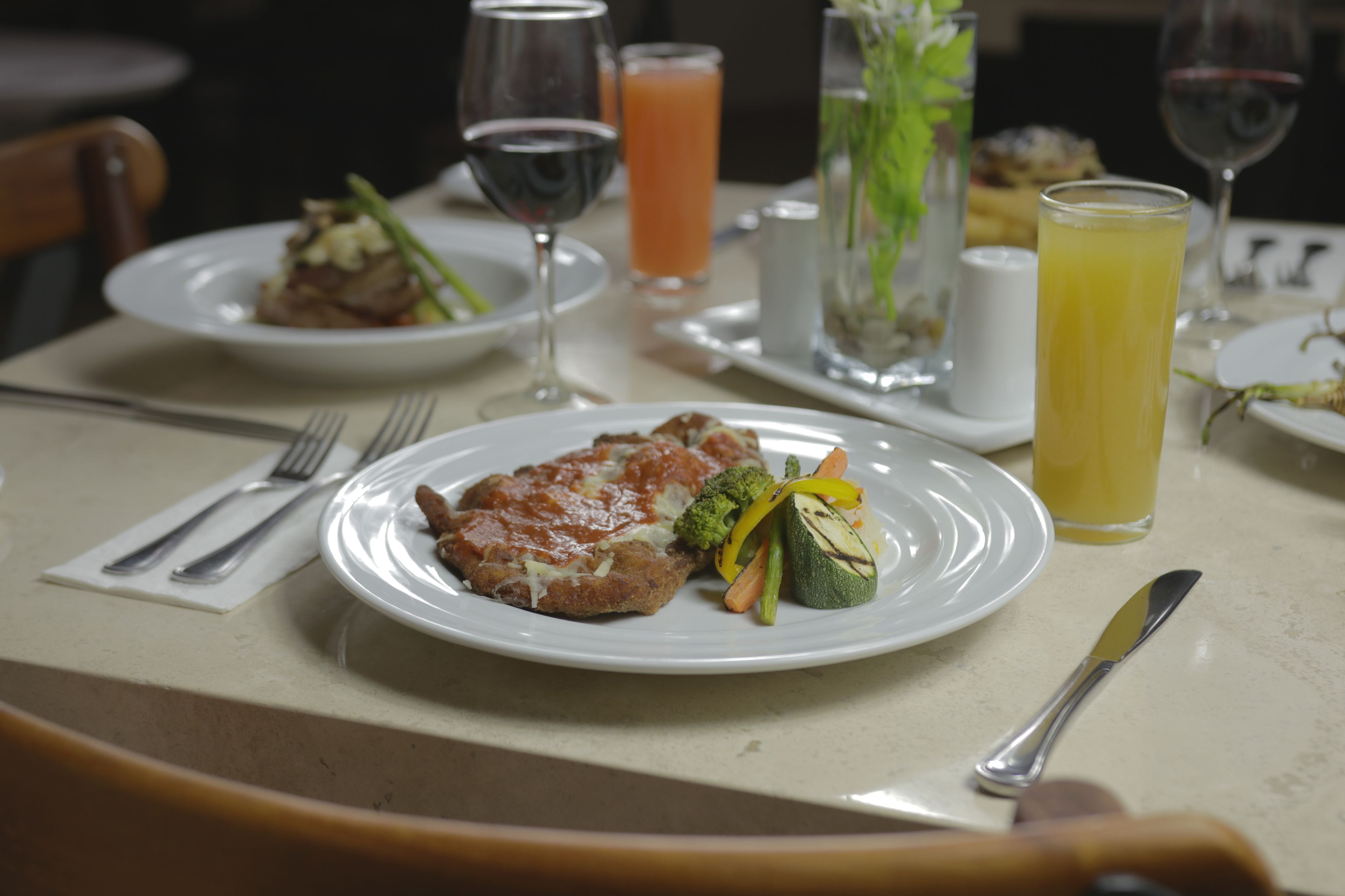 Una mesa de comedor con platos de comida, cubiertos y vasos de bebidas.