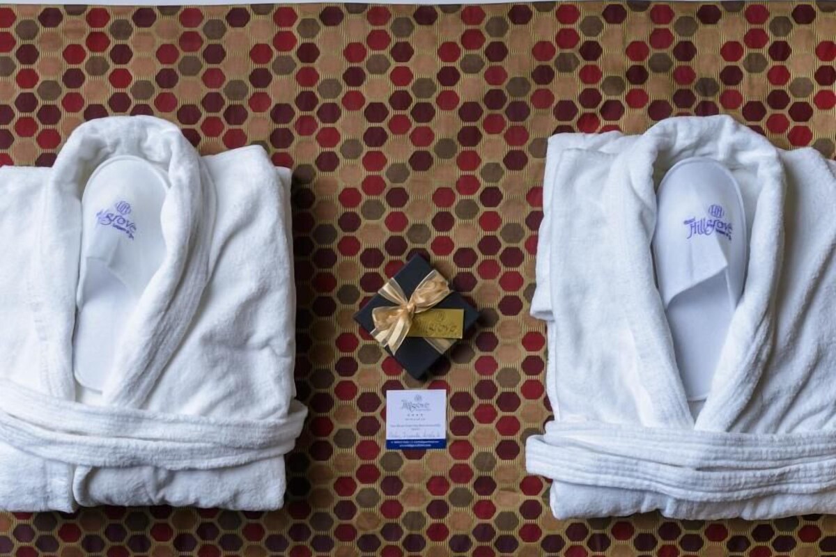Two white robes with a logo, a gift box, and a price tag on a patterned wall.