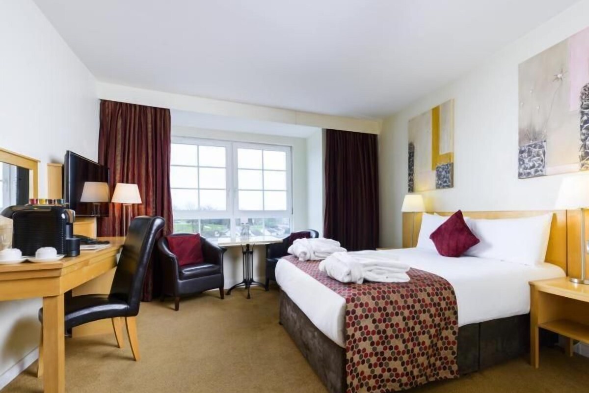 A hotel room with a bed, desk, chair, and a window.