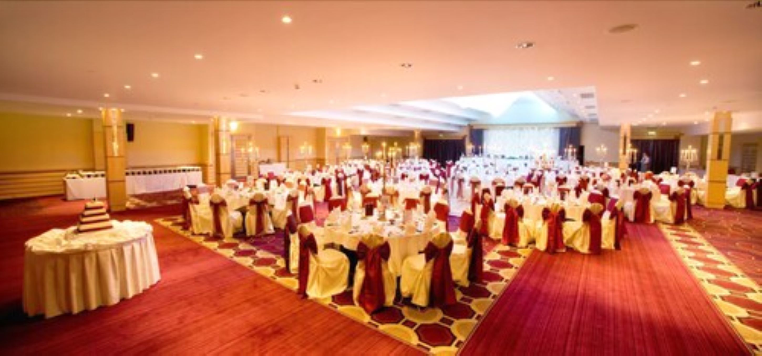A banquet hall with round tables and chairs, a stage, and a red carpet.