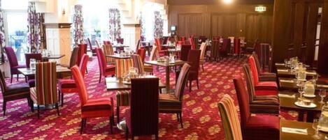 A restaurant with multiple tables and chairs, a patterned carpet, and a warm ambiance.