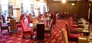 Ein Restaurant mit mehreren Tischen und Stühlen, einem gemusterten Teppich und einer gemütlichen Atmosphäre.
