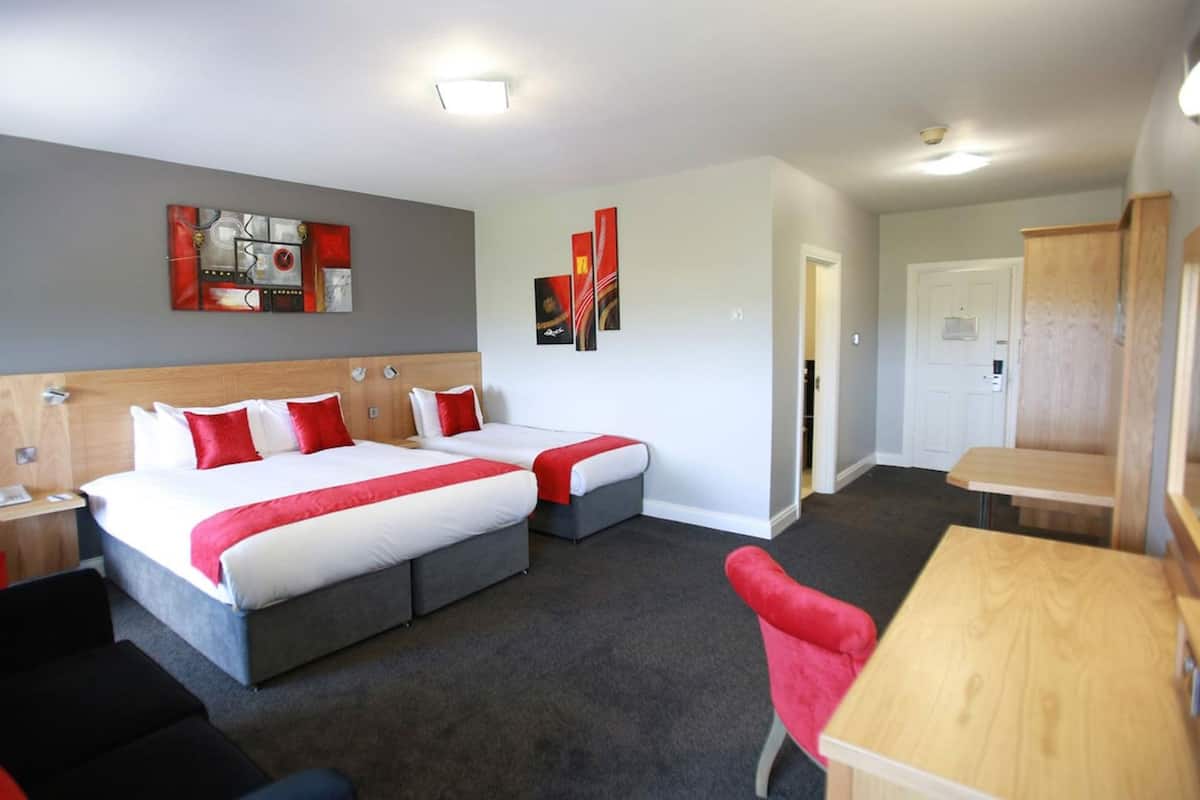 Habitación de hotel con dos camas, un escritorio, una silla y un sillón rojo.