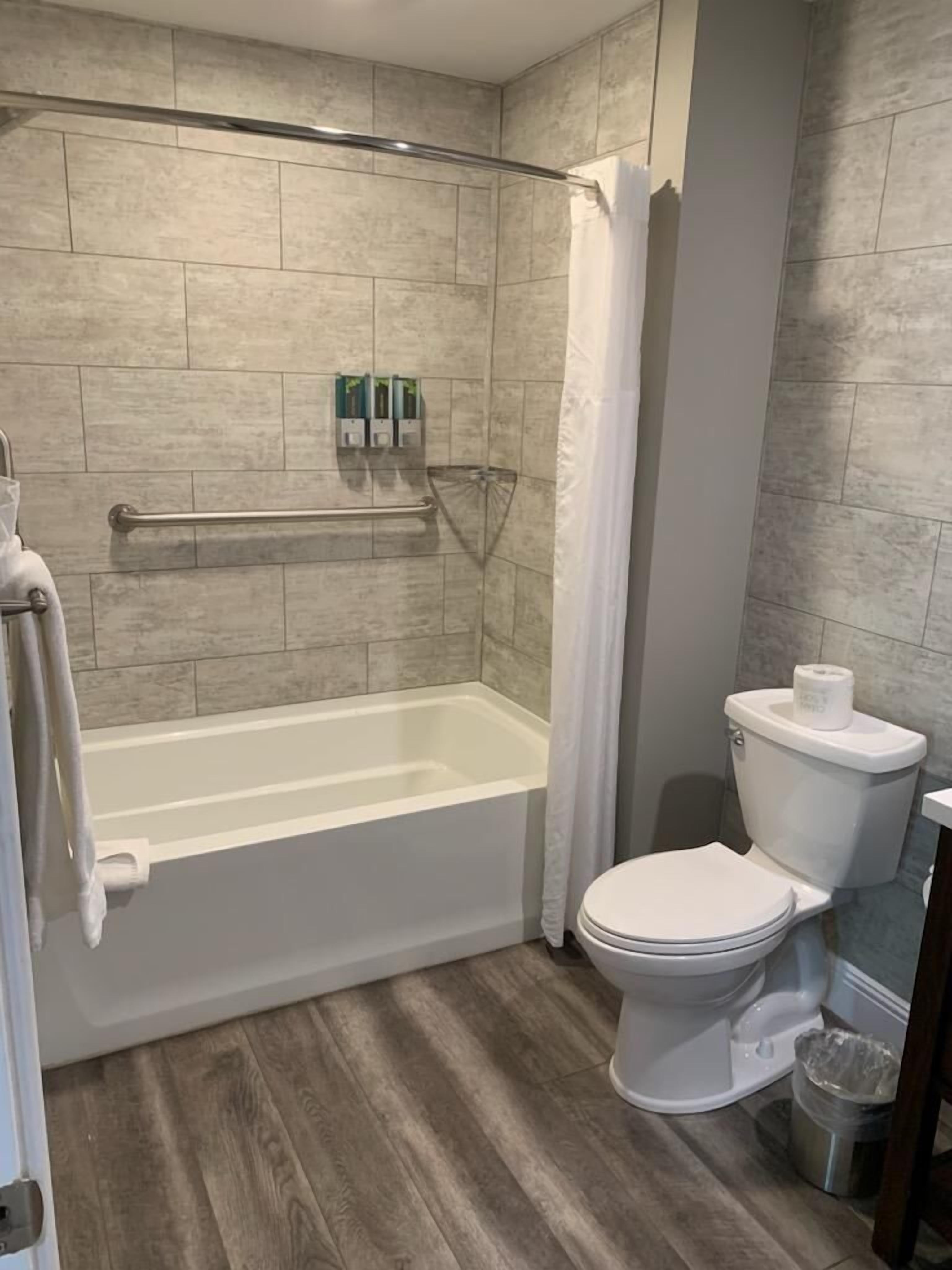 A modern bathroom with a walk-in shower, grab bars, a toilet, and a trash can.