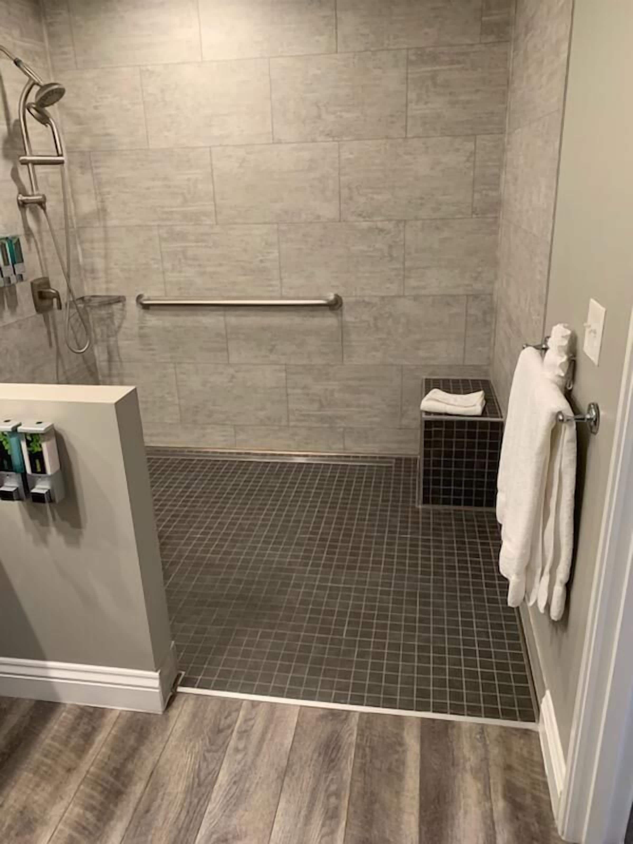 Een badkamer met een douche, een handgreep, een klein plankje met een handdoek en een toilet.