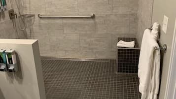 A bathroom with a shower, a handrail, a small shelf with a towel, and a toilet.