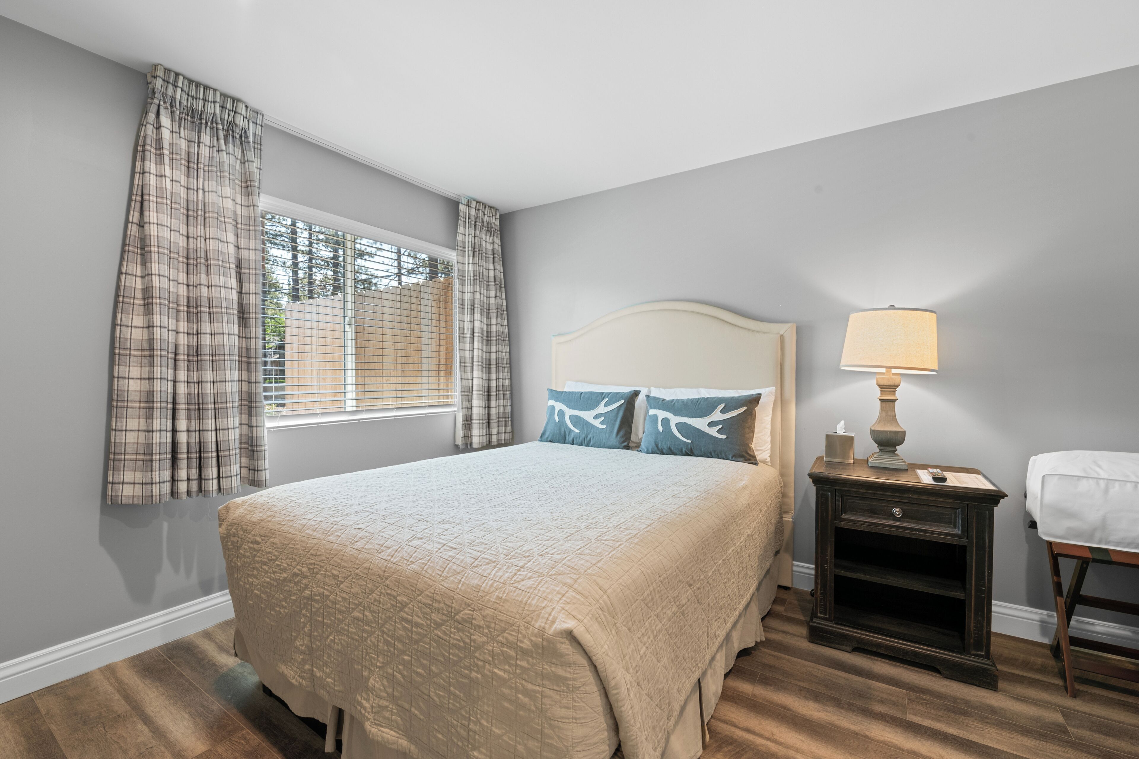 A bedroom with a large bed, a nightstand with a lamp, and a window with curtains.
