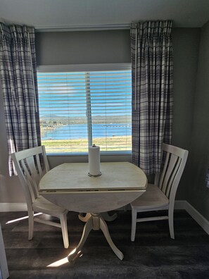 A dining area with a round table and four chairs, a window with blinds, and plaid curtains.