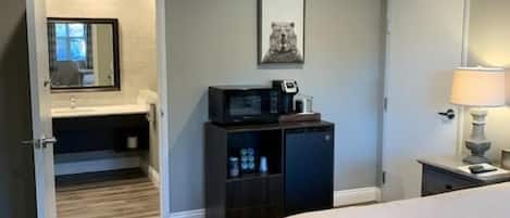 Una habitación de hotel con una cama, un escritorio con una computadora, un microondas y un mueble pequeño.
