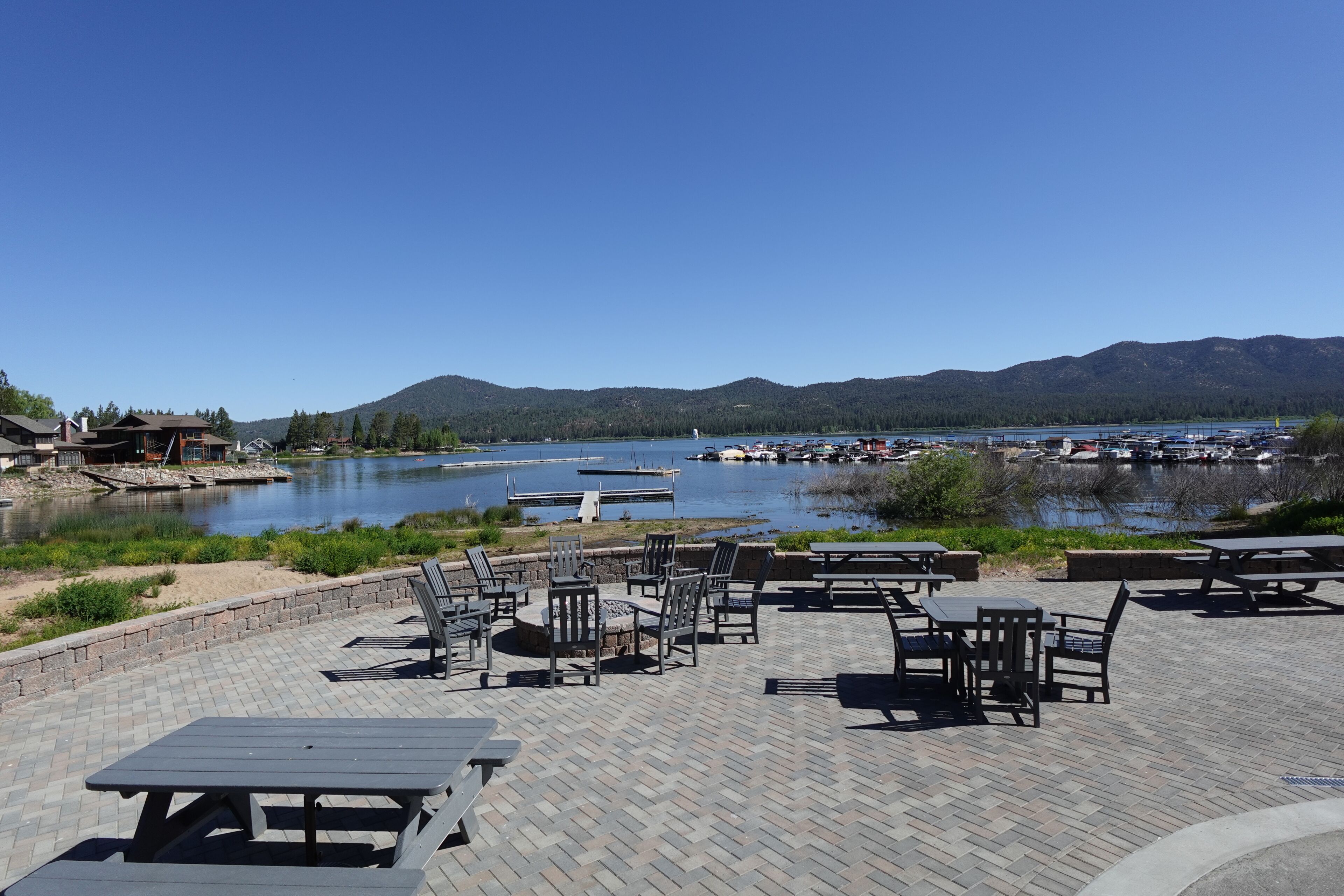 An outdoor seating area with tables and chairs overlooking a lake with boats and docks.