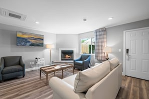 A living room with a fireplace, a sofa, a chair, a coffee table, and a painting on the wall. - Big Bear Frontier (Big Bear Lake)
