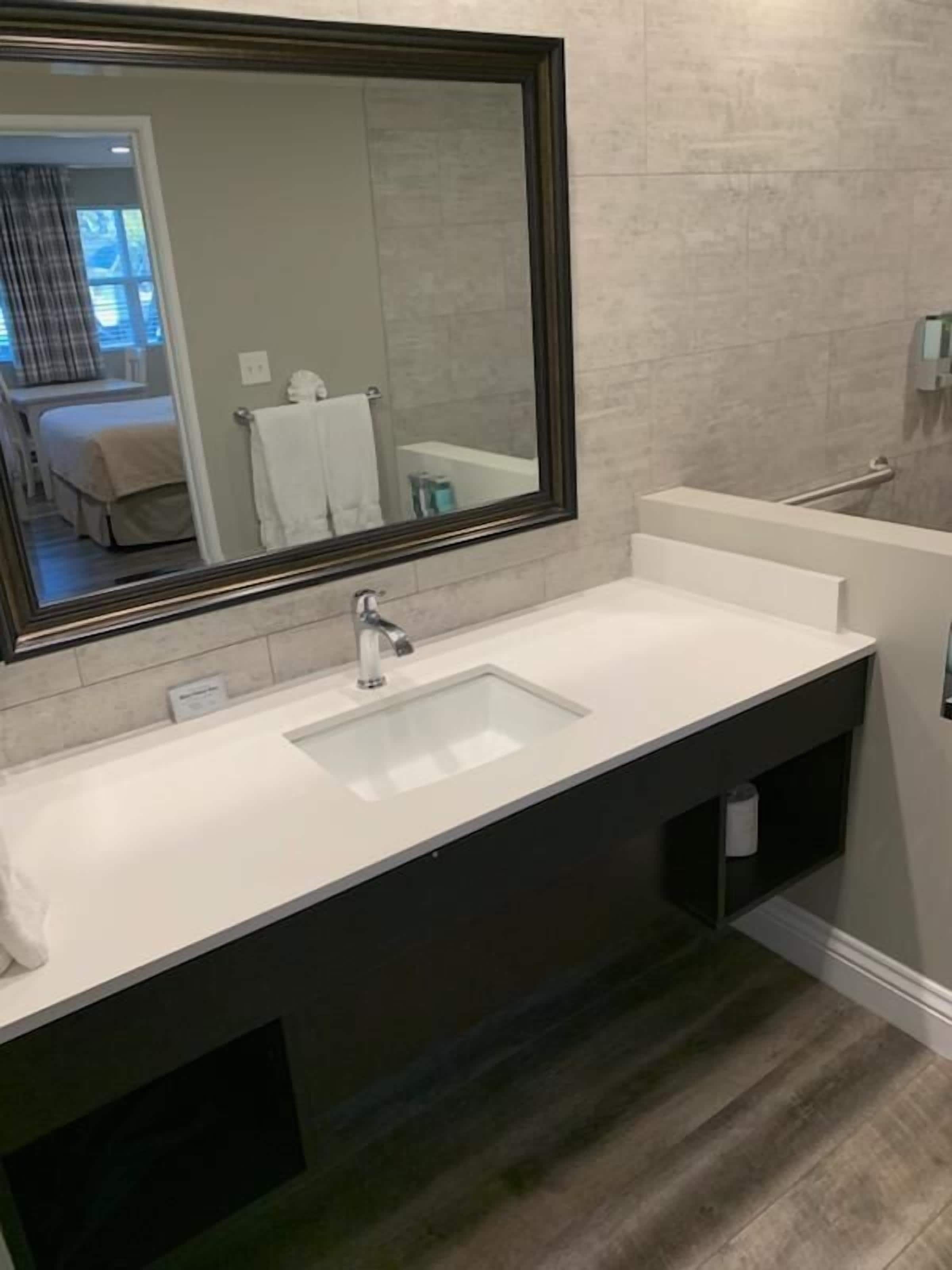 Une salle de bain moderne avec un grand miroir, un lavabo blanc et un meuble-lavabo foncé.