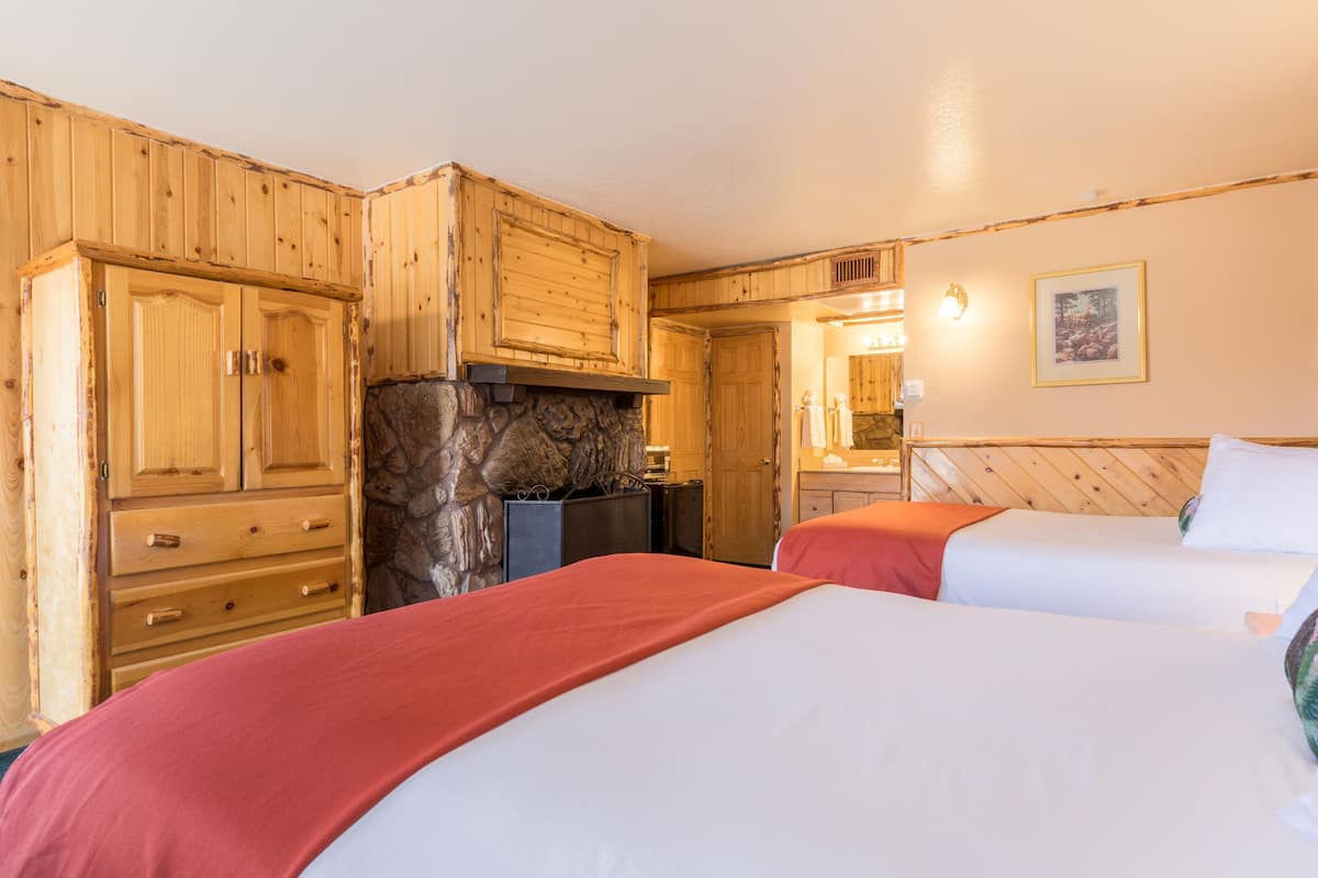 A room with wooden cabinets, a stone fireplace, two beds with red and white bedding, and a framed picture on the wall.