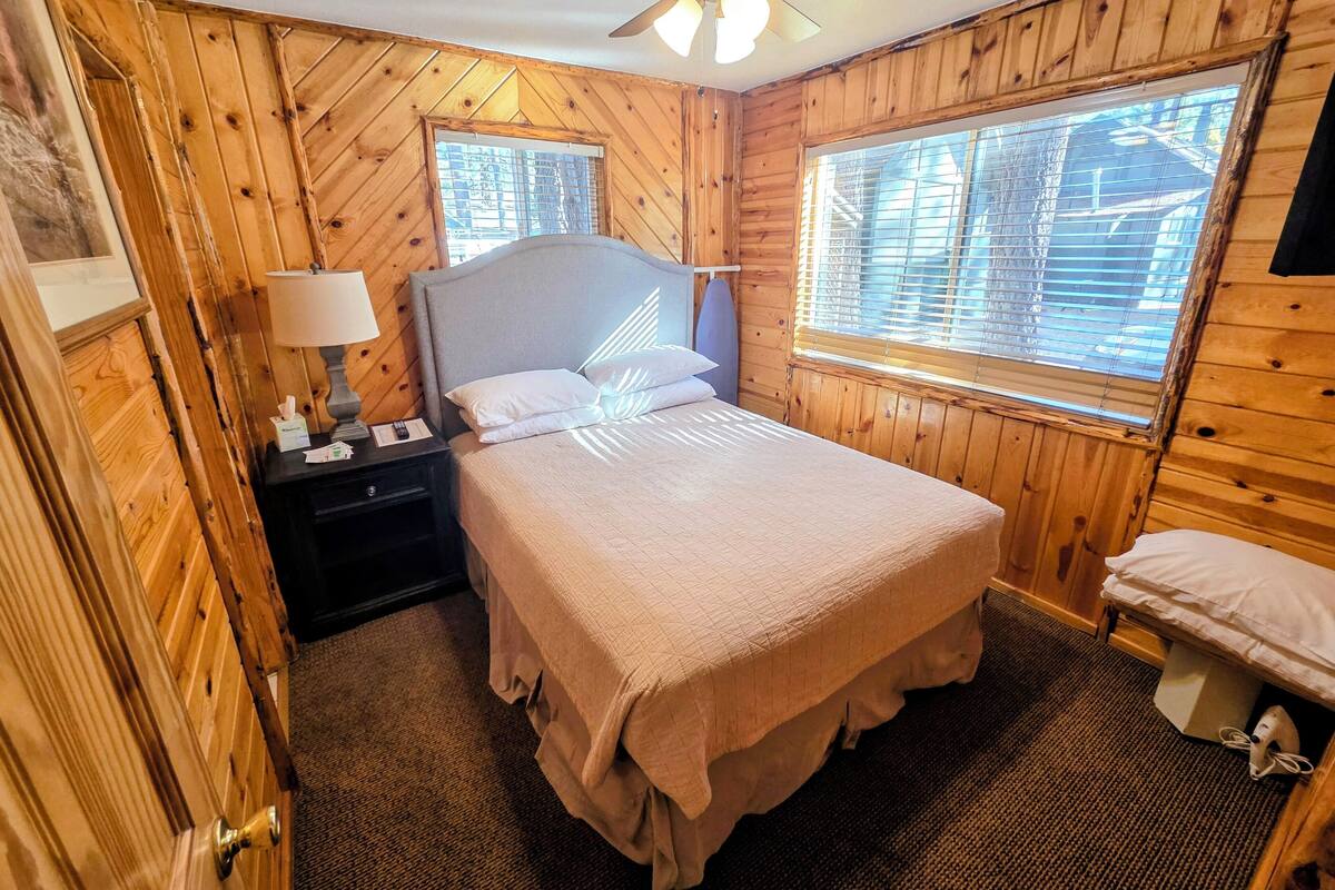 A wooden-paneled bedroom with a bed, nightstand, lamp, and a ceiling fan.