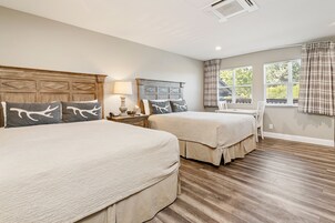A bedroom with two beds, a nightstand, a lamp, and a window with curtains.