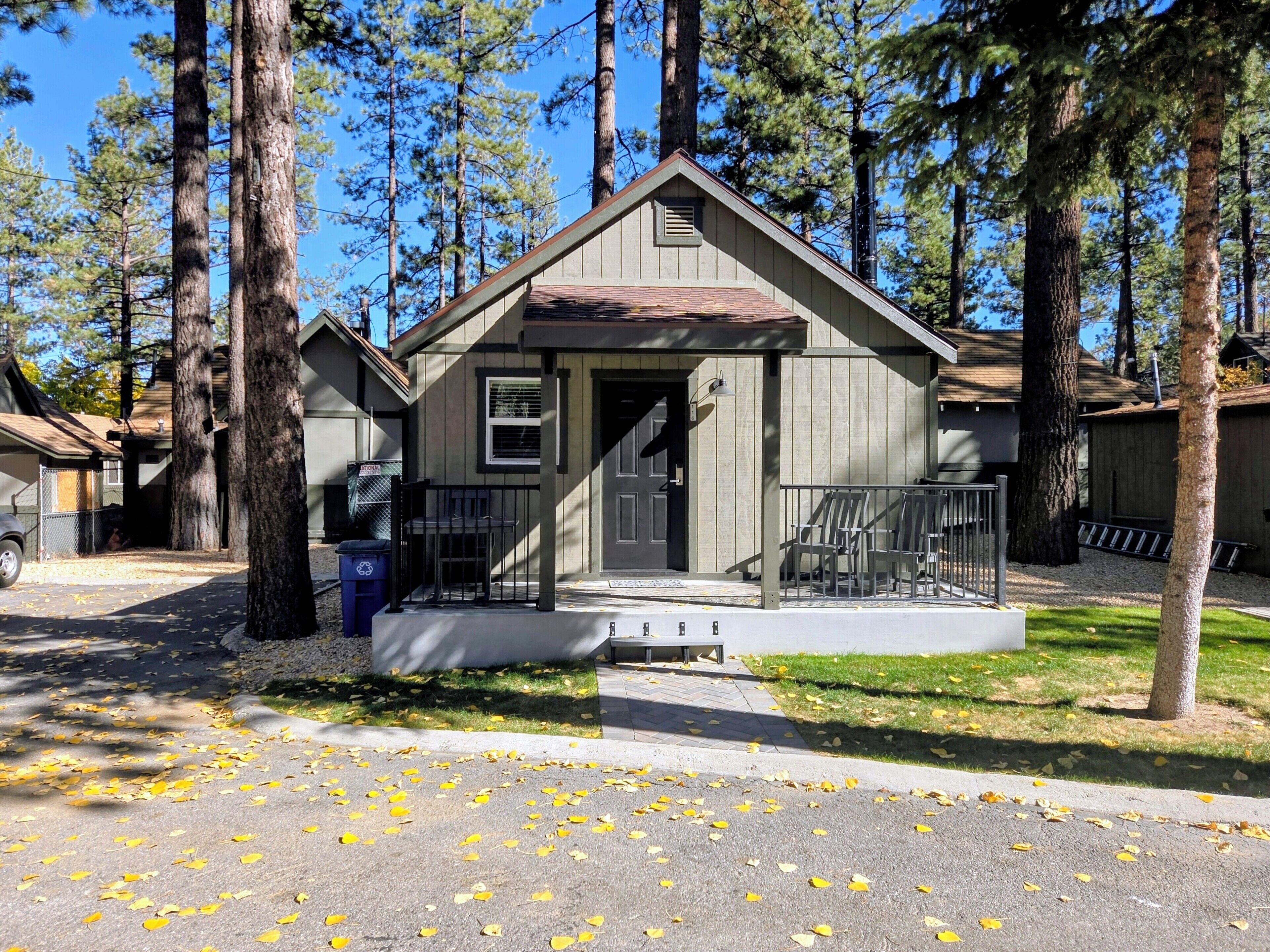 A small cabin with a front porch, surrounded by tall trees.
